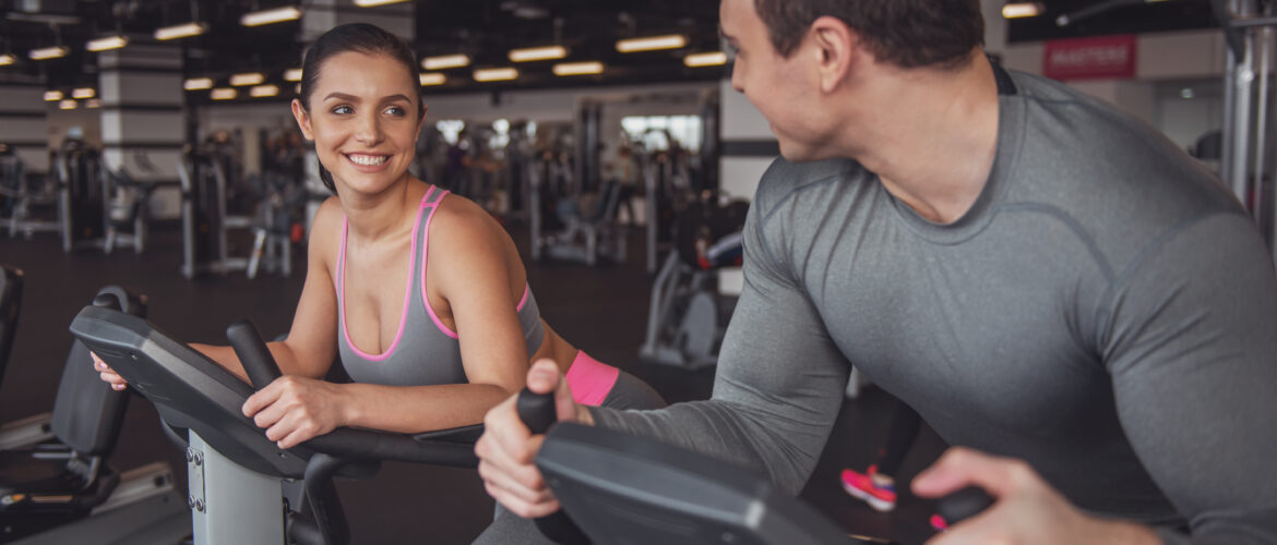 Attractive young people working out on an exercise bike in gym and smiling